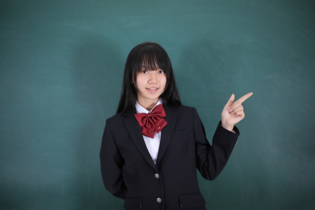 黒板の前にいる制服を着た女子高生の写真